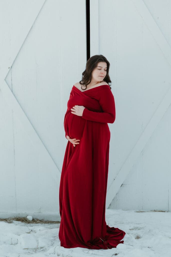 Beautiful expecting mother holding baby bump during an outdoor maternity session in nature during a NJ snowy day.