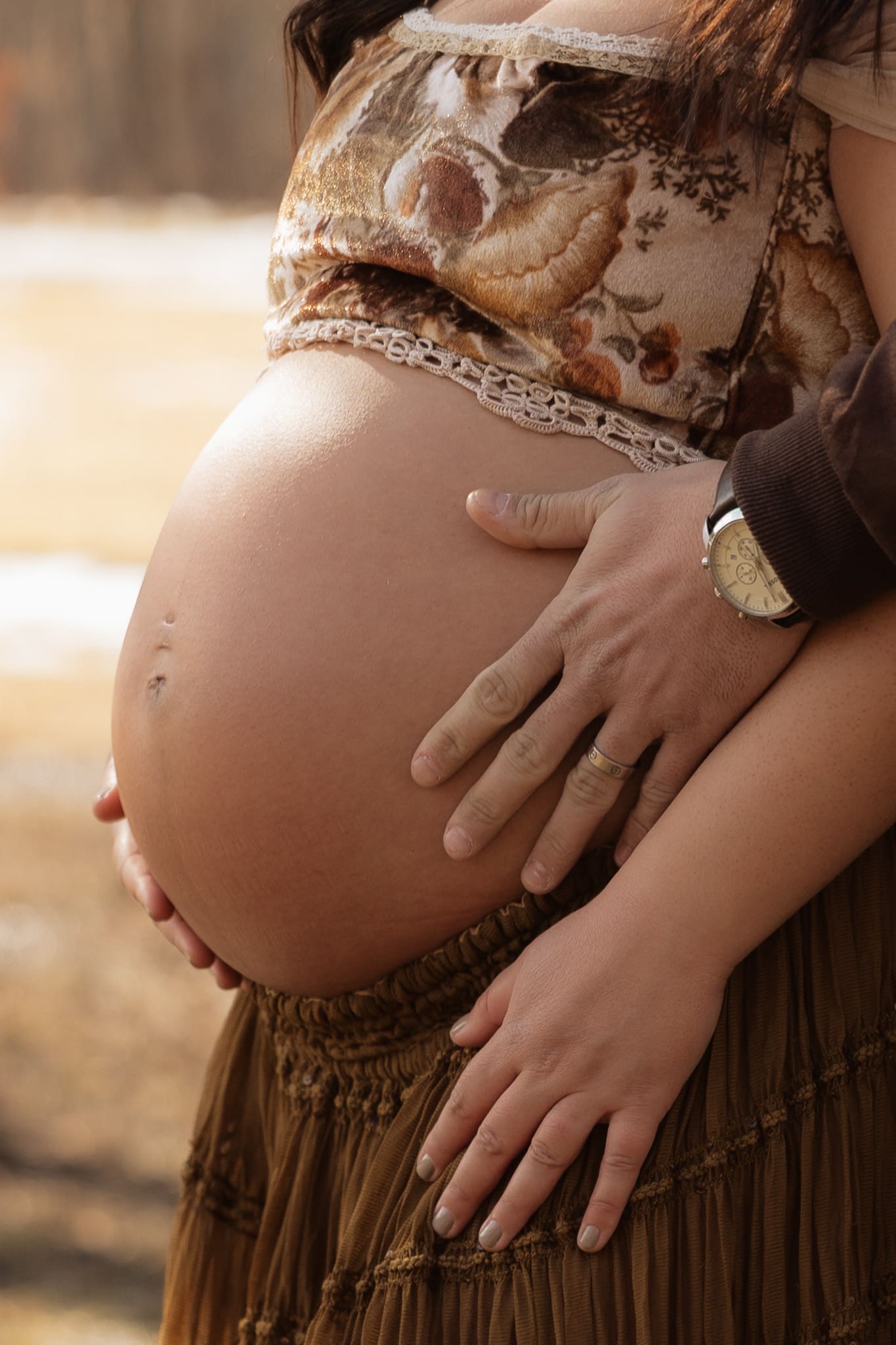 Close-up of pregnant woman’s baby bump with partner’s hands during a warm outdoor maternity photoshoot in New Jersey