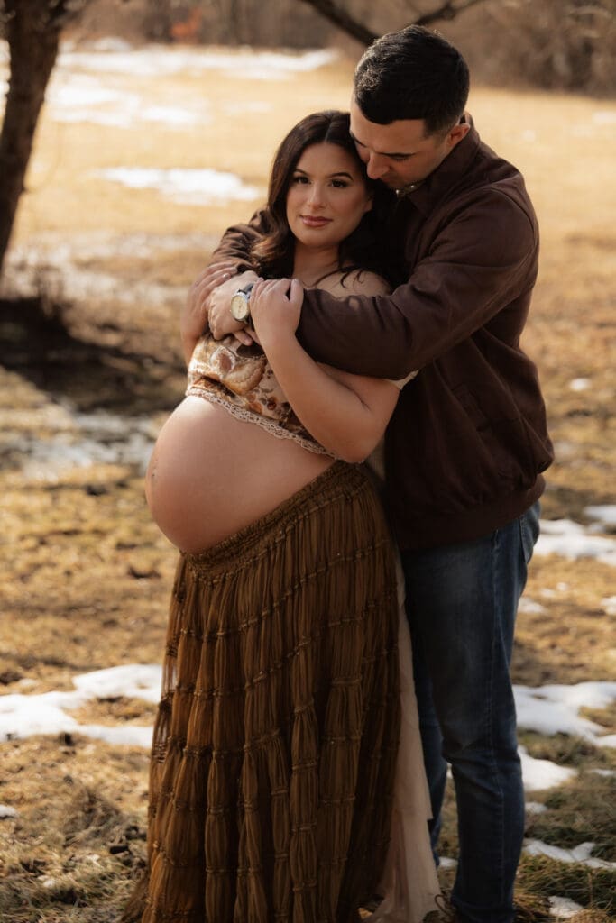 Pregnant woman posing for outdoor maternity photos in warm natural light with partner on a farm in NJ.